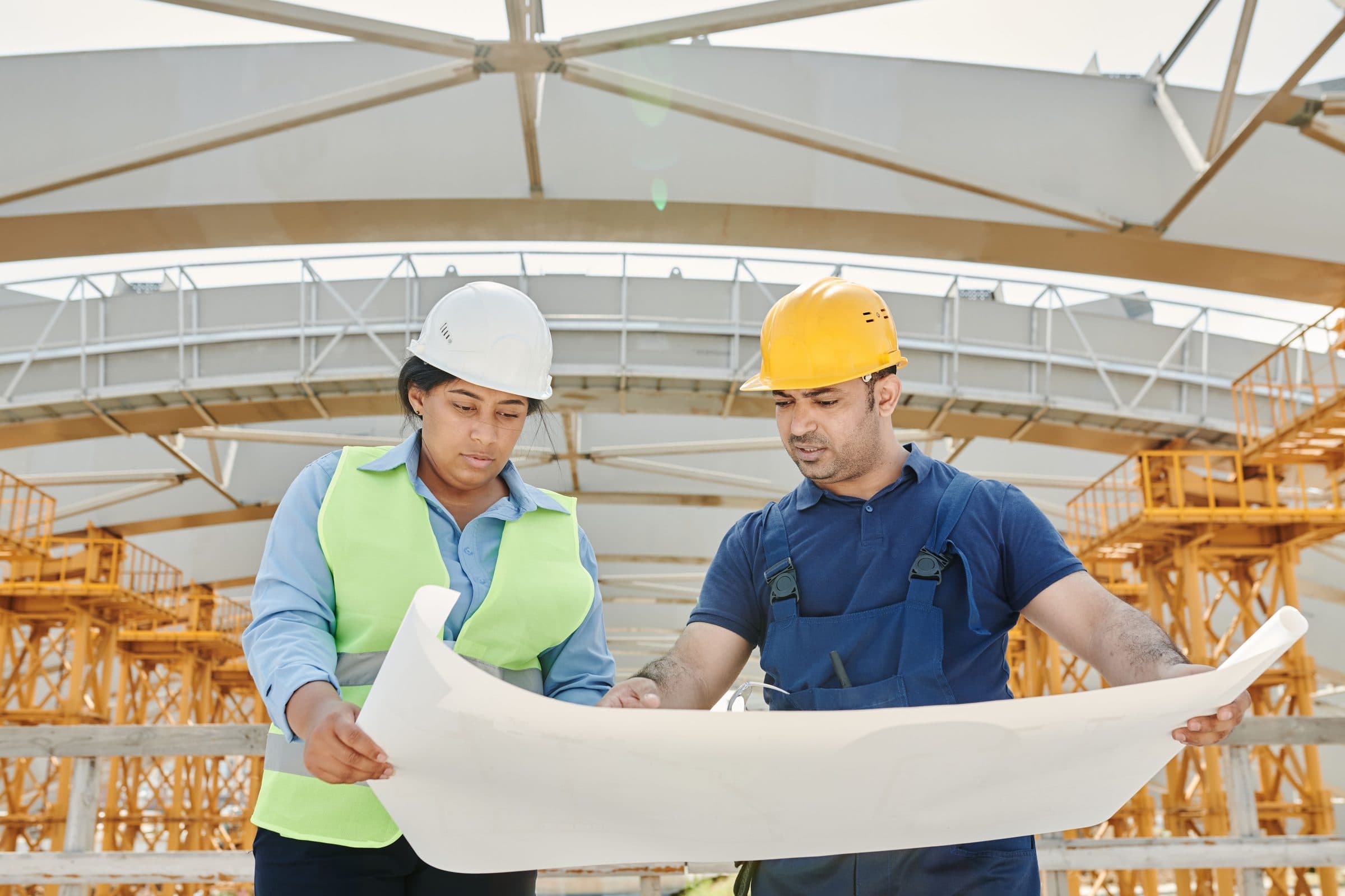 Engineers in safety helmets reviewing blueprints at a construction site